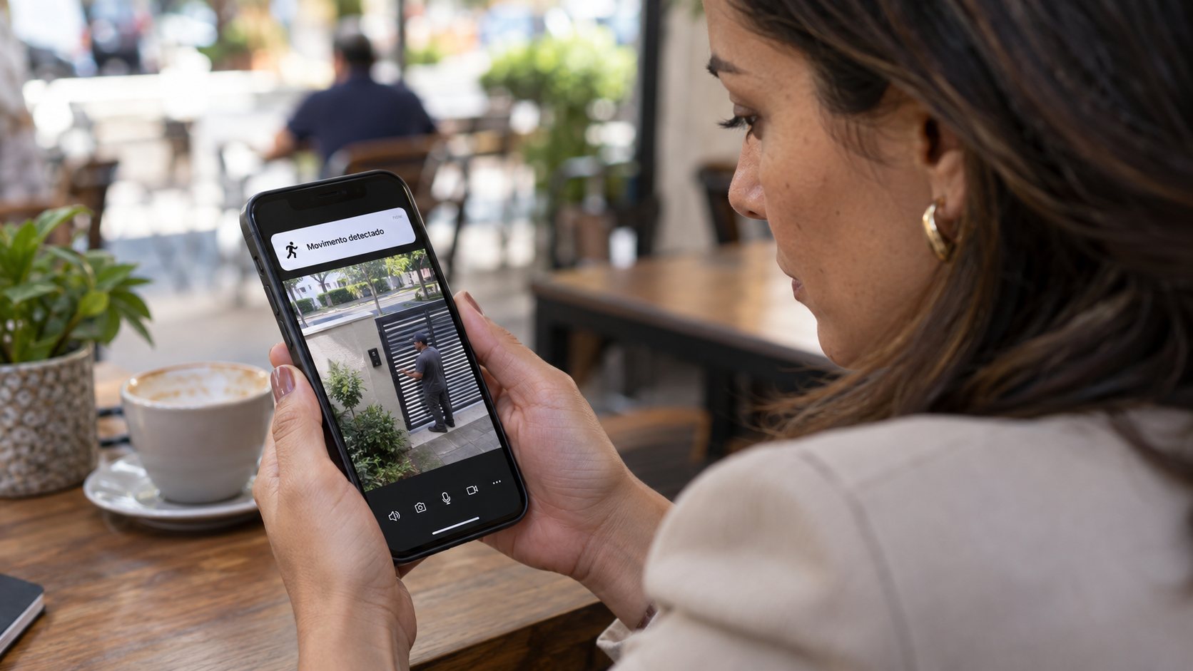 Mulher num café olhando no celular o alerta de movimento detectado pela câmera do portão de casa